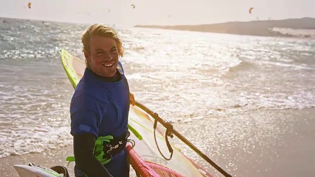 SLO MO肖像微笑的男子带着他的风帆冲浪出水到阳光沙滩视频素材