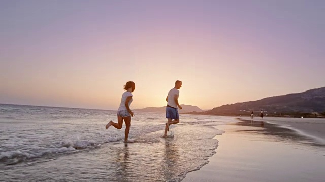 日落时分，父亲和女儿在海滩上互相泼水，然后跑步视频素材