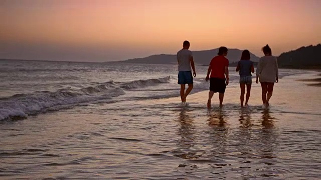 妈妈，爸爸和两个十几岁的孩子在日落的海滩上散步视频素材