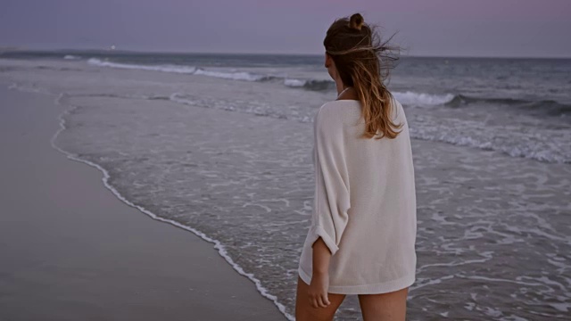SLO MO女人独自走在日落的海滩上视频素材