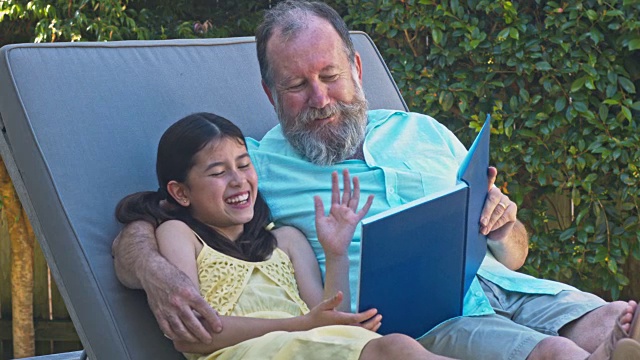 快乐的孙女和爷爷在躺椅上看书视频下载