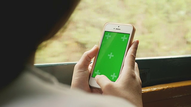 在火车上移动到其他地方时，智能手机上的绿色屏幕上的亚洲妇女的手的特写-色度键视频下载