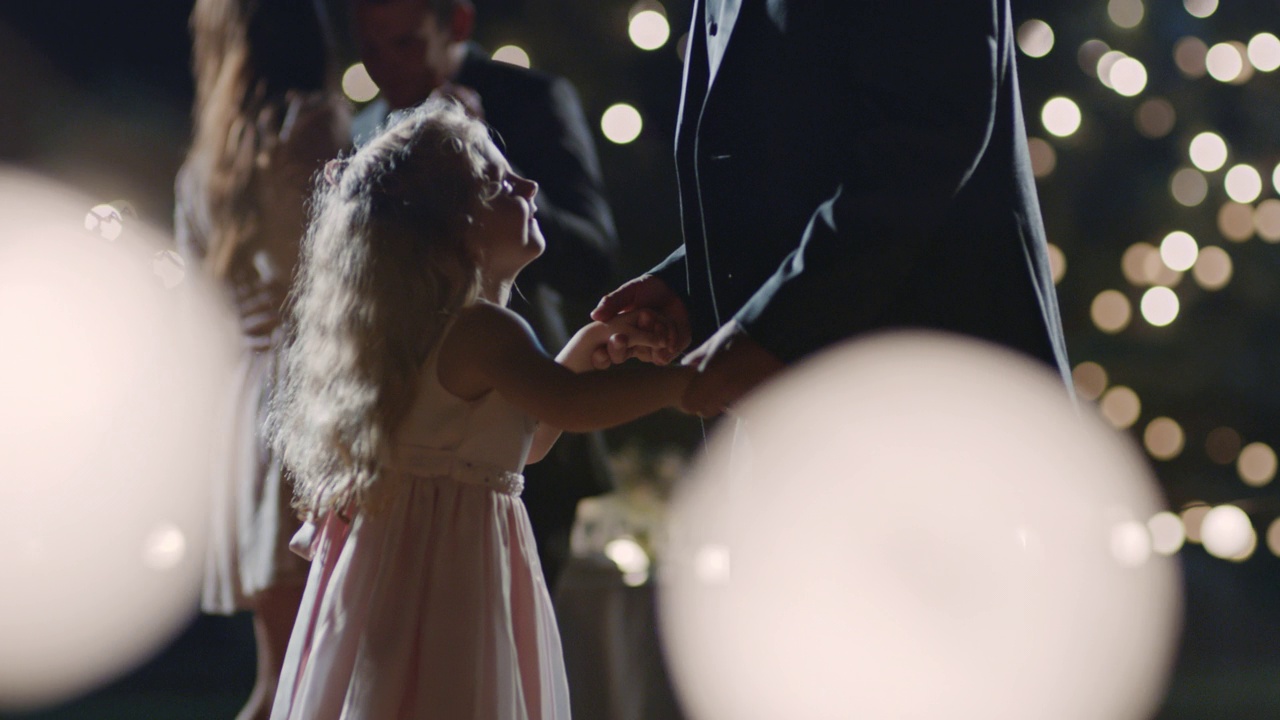 在婚宴上，一个小女孩抬头微笑着和她的父亲跳舞。视频素材