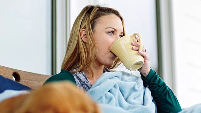 铜。睡狗躺在毯子下，旁边的年轻女子喝咖啡在户外露台沙发上。视频下载