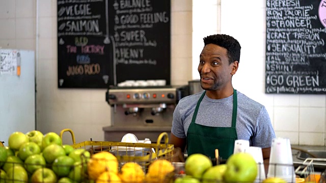 在果汁吧工作的黑人推销员传递一个绿色果汁给一个看起来非常高兴和微笑的不认识的顾客视频素材