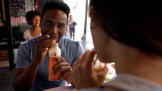 快乐的黑人男子在一个果汁酒吧与一个不认识的女人聊天，同时享受果汁视频素材