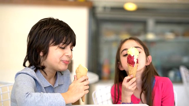 哥哥和姐姐在冰淇淋店享受着冰淇淋，看起来很开心，谈笑风生视频素材