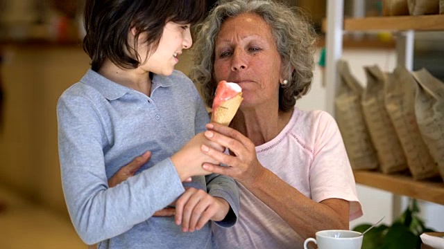 慈祥的祖母拥抱着她的孙子，孙子和她分享他的冰淇淋都很快乐视频素材