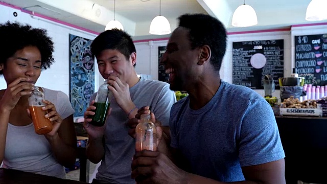 亚洲和黑人朋友在果汁吧与瓶装果汁祝酒，大笑和玩得很开心视频素材