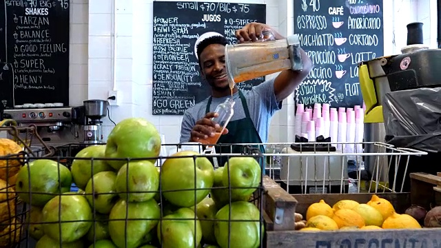 一个快乐的黑人在一个果汁吧工作在一个瓶子果汁看起来很高兴视频素材