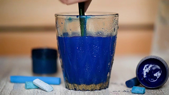 在一个透明的玻璃杯中加入一滴蓝色颜料并搅拌。水是彩色视频下载