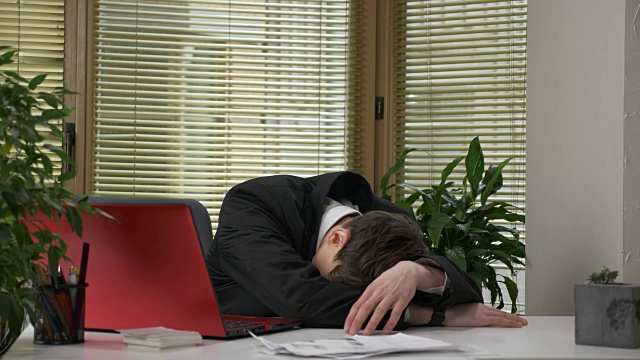 一个穿着西装的年轻人正坐在办公室里，用笔记本电脑工作，疲惫不堪，无聊地睡着了。60 fps视频下载