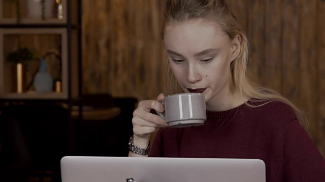 年轻的女人坐在笔记本电脑后面，一边喝着咖啡工作一边思考视频素材