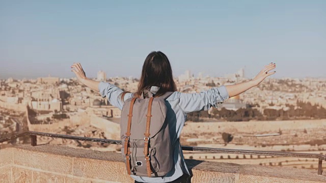 快乐的欧洲女游客举手。以色列耶路撒冷。背着背包的女孩去看旧城的全景。4 k视频素材