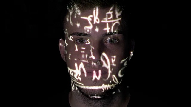 杰出的奥林匹克数学家坐在黑暗的背景上，公式投射在他的脸上视频素材
