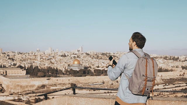 游客男性拍摄耶路撒冷全景照片。一个背着背包的男人拿着智能手机站在甲板边缘。以色列4 k视频素材