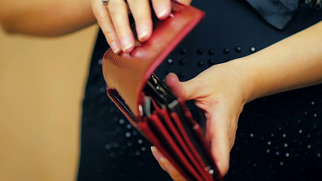 一个年轻女孩的特写关闭一个红色皮革钱包，其中有现金在慢动作视频素材