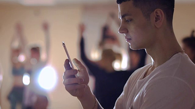 一个年轻人用手机看他的朋友在模糊背景下跳舞视频下载
