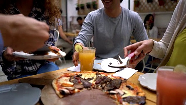 一群朋友在一家意大利餐厅分享披萨，他们看起来很开心，微笑着切披萨视频素材
