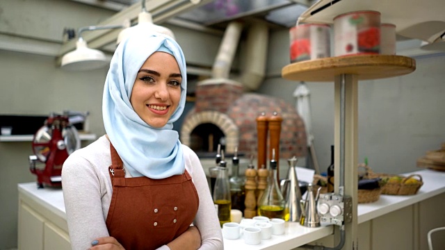 一个美丽的穆斯林妇女的餐馆老板看着镜头微笑着双臂交叉视频下载