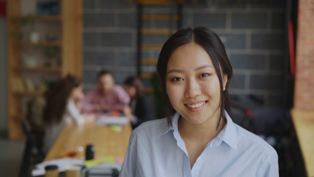 亚洲自信女商人的肖像，看着相机和微笑，她的多民族团队在现代阁楼办公室的初创项目视频下载