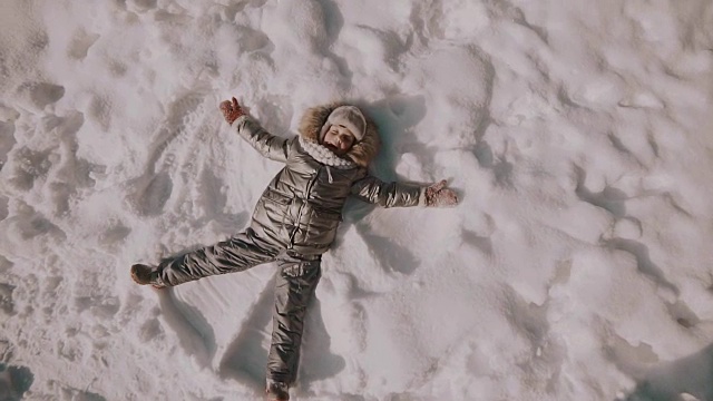 一个小女孩在雪中堆雪天使。俯视图视频素材