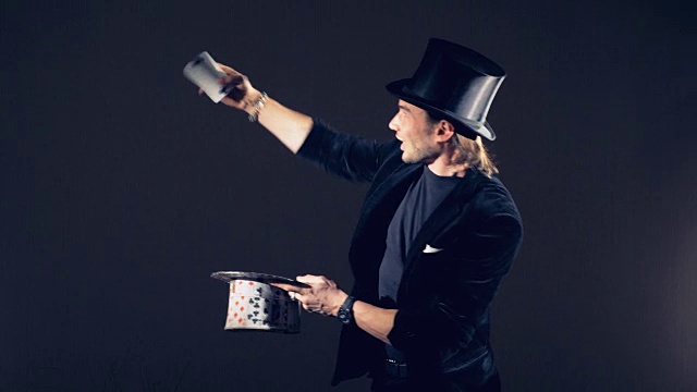 一个男性魔术师正在用卡片表演魔术，并把它们放在一个卡片礼帽里视频下载