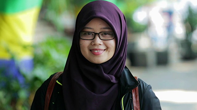 美丽的东南亚穆斯林妇女戴着头巾在镜头前微笑，有三种色调(蓝-橙，对比，和原始)视频下载
