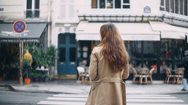 年轻美丽的女人在巴黎过马路的背影，法国。穿着斗篷走在街上的时尚女性视频下载