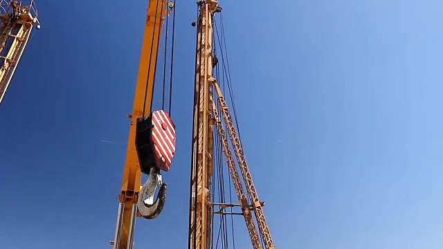 红色和白色条纹的移动式起重机钩飞过建筑工地视频下载