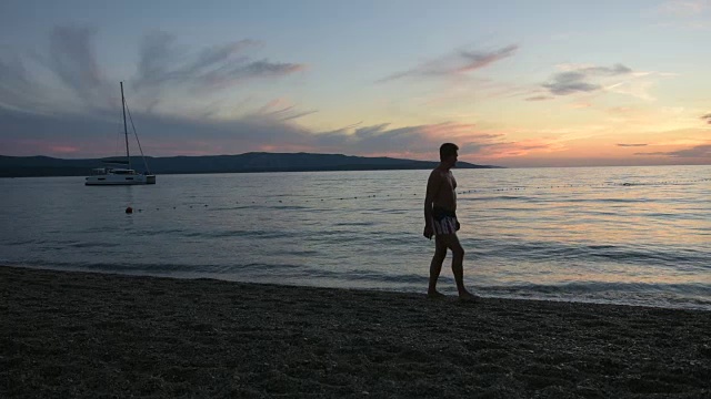 一个成年人在海滩上散步，欣赏夕阳下的大海视频下载