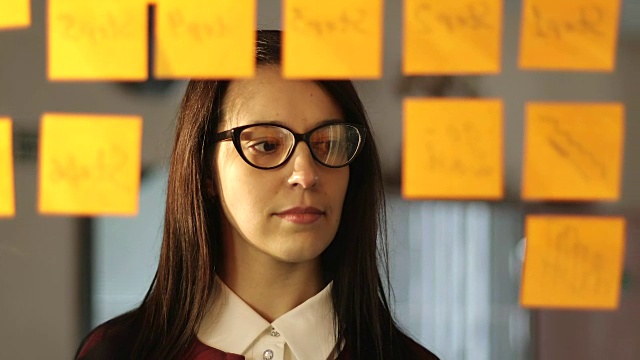 一位戴眼镜的年轻女商人正在办公室的玻璃上贴小贴纸。视频素材