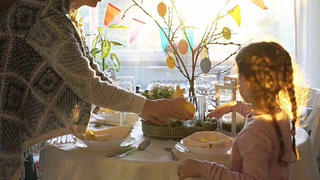 一位妇女和她的小女儿正在用兔子和鸡蛋装饰复活节的餐桌视频素材