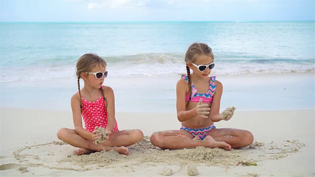 可爱的小女孩在沙滩上玩沙子。孩子们坐在浅水里做沙堡视频素材