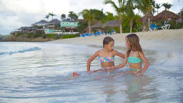 可爱的小女孩们在沙滩上放松，在浅水里玩耍视频素材