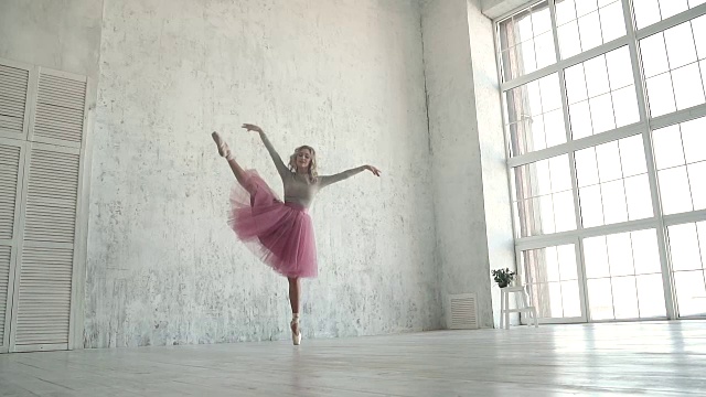 女孩以一扇巨大的窗户为背景跳舞。在工作室里表演脚尖旋转的芭蕾舞者。穿着经典芭蕾短裙和脚尖的芭蕾舞者视频素材