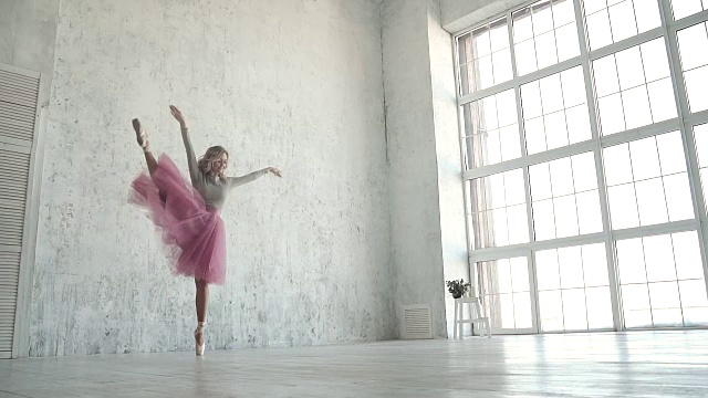 穿着经典芭蕾短裙和脚尖的芭蕾舞者。在工作室里表演脚尖旋转的芭蕾舞者。一个优雅的女孩在一个巨大的灯光窗户的背景下跳舞视频素材