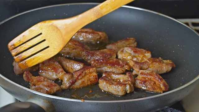 把肉片放在煎锅里煎。煎锅里的肉和木铲混合。肉在原汁中煮视频下载