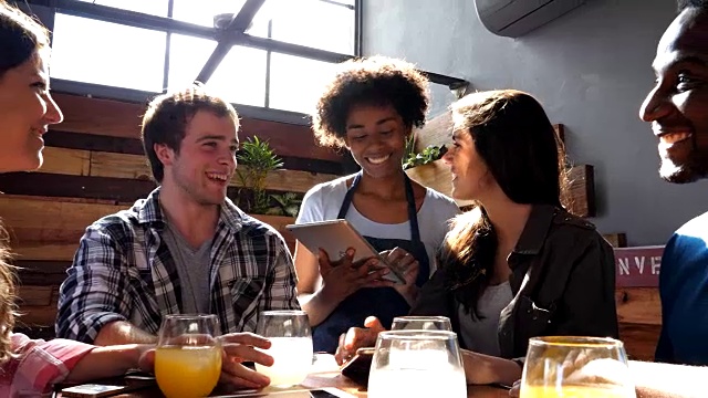 友好的黑人女服务员正在用平板电脑为一群不同的朋友点餐视频素材