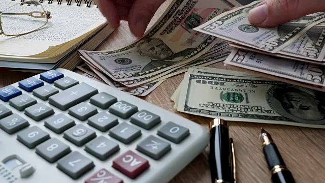 一个男人在办公桌上数钱。美元钞票和计算器。储蓄和家庭预算。视频素材