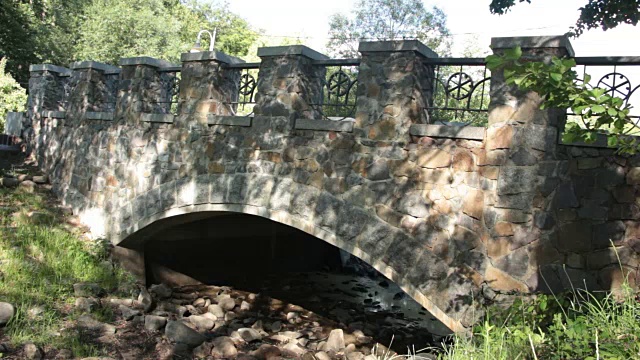 在一个晴朗的夏日，公园里的石桥在一条干涸的小溪上视频下载