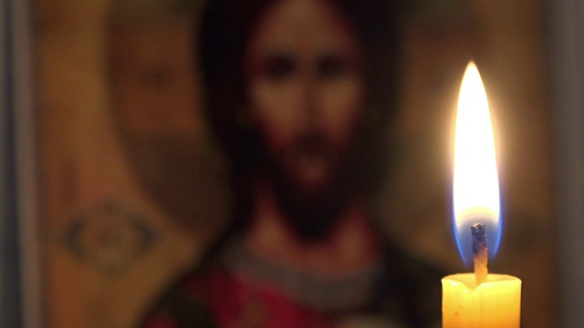 在一间黑暗的房间里，一支燃烧着的蜡烛，背景是正统的圣像视频素材
