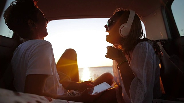 一对年轻夫妇在汽车后备箱里度假。背景是大海和日落。视频素材