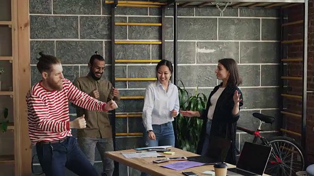 多民族创业公司的同事在现代的办公室里跳舞，扔文件，庆祝项目的成功视频素材