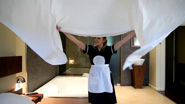 漂亮的管家在酒店整理床铺，微笑着把床单铺在床上视频素材