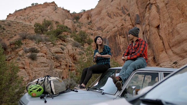 在摩押登山之旅中，一名年轻男子和一名女子坐在车顶上，一边吃三明治一边聊天。视频素材
