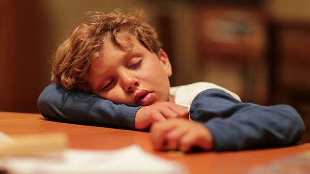 瞌睡的孩子累了头枕着桌子睡着了。小男孩在漫长的一天之后睡着了，因为一天的活动而筋疲力尽视频素材