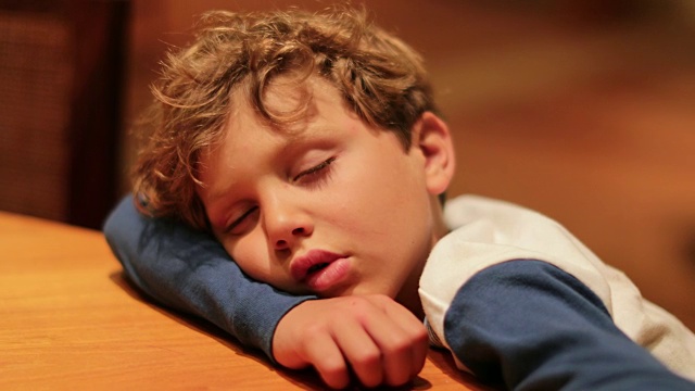 疲惫困倦的孩子耷拉着脑袋躺在桌子上，耷拉着身体，疲惫地恢复着精力视频下载