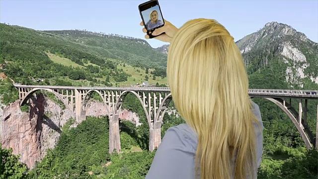 金发女子用智能手机自拍，背景是一座拱桥视频下载
