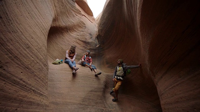 摩押攀爬之旅的一群朋友在美丽的槽状峡谷的砂岩墙上休息。视频素材